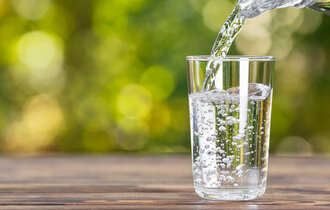Water,From,Jug,Pouring,Into,Glass,On,Wooden,Table,Outdoors