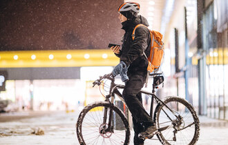 Ein Mann auf einem Fahrrad steht in einer verschneiten Stadt und hat sein Handy in der Hand.