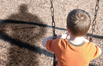 trauriges Kind auf der Schaukel mit Schatten eines Erwachsenen