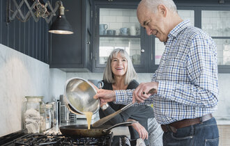 Älteres Ehepaar steht in der Küche und kocht gemeinsam.