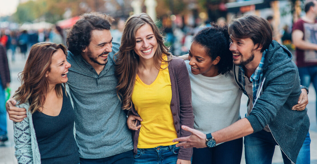 Eine Gruppe von fünf jungen Leuten, die nebeneinander laufen und sich dabei im Arm haben.