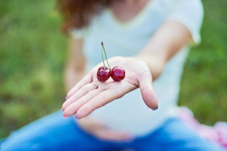 Pregnant woman hold cherries in garden. Concept for healthy food and pregnancy.
