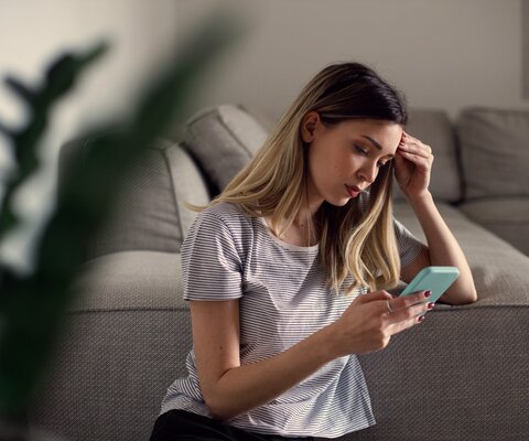 Serious thoughtful young woman holding smartphone