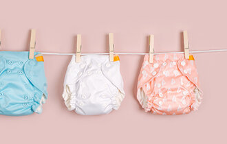 Eine Wäscheleine mit drei aufgehängten Babywindeln in blau, weiß und rot.