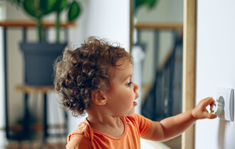 Kleinkind spielt mit Steckdose in der Wand.