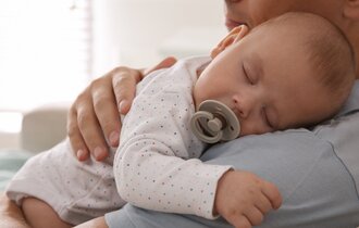 Vater hält sein schlafendes Baby im Arm.