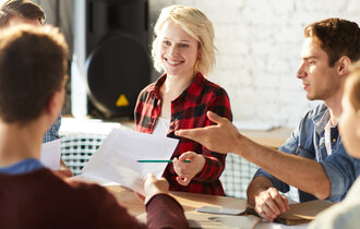 Drei Männer und zwei Frauen sitzen im Büro an einem Tisch zusammen und diskutieren Ideen.