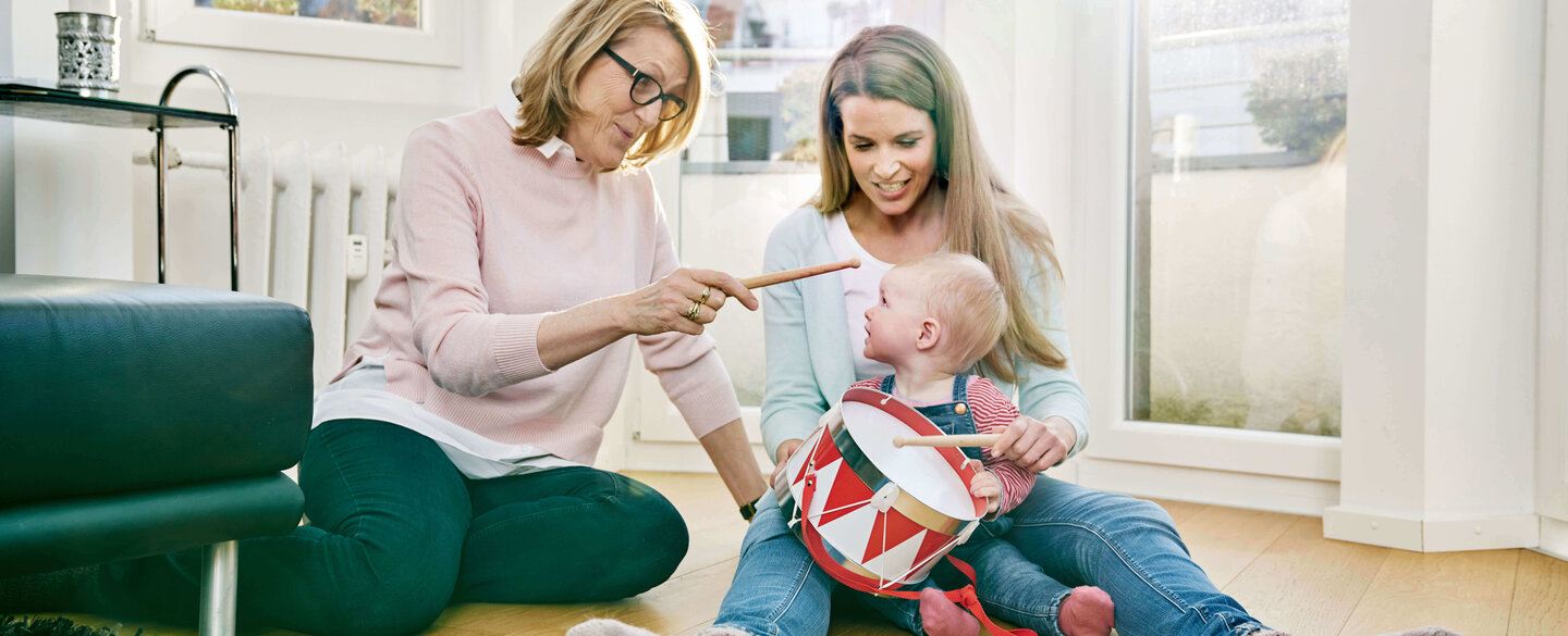 Grandmother, mother and baby girl sitting on floor playing drums