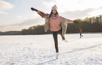 Frau mit Schlittschuhen tanzt auf Eislauffläche mit Menschen im Hintergrund.