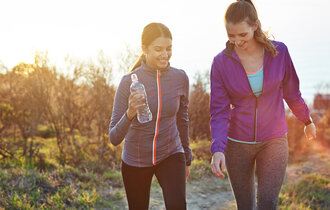 Zwei Frauen joggen durch eine herbstliche Landschaft.