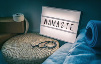 Blaue Yogamatte sowie weiteres Zubehör liegen vor einem beleuchteten Schild mit der Aufschrift "Namaste".