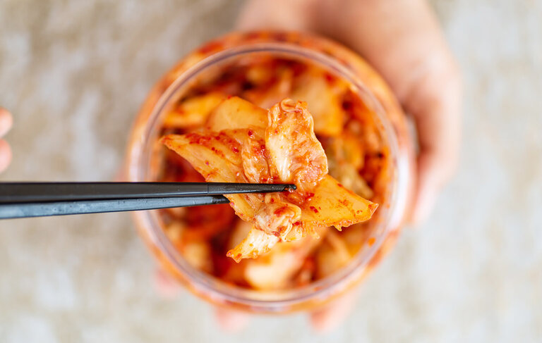 1325417759 Kimchi in einem Glas von oben. Zwei chinesische Stäbchen holen ein Stück heraus.