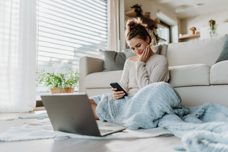 Young woman resting in living room with smartphone and laptop.