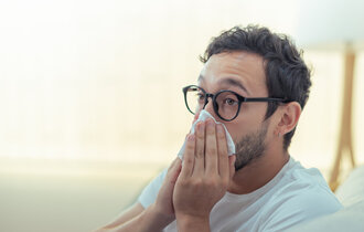 Ein Mann mit Brille putzt sich die Nase.