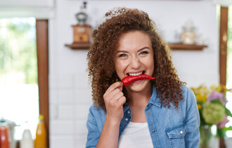 Young woman holding red pepper in her mouth