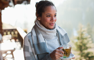 Eine lächelnde Frau trinkt draußen im Stehen einen Tee.