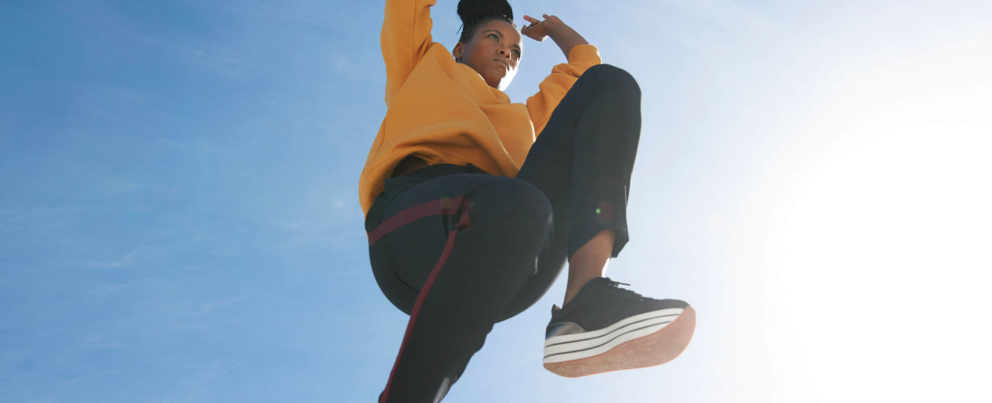 Junge Frau mit gelbem Pullover, die an einem sonnigen Tag gen blauem Himmel springt