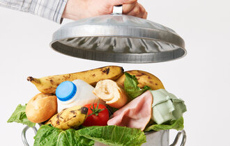 Hand packt Deckel auf Mülltonne voller Lebensmittelabfälle.