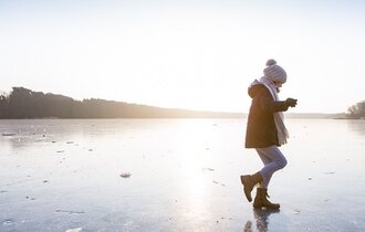 Kind in Winterkleidung läuft auf zugefrorenem See.