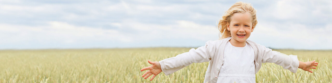 Ein blondes Mädchen rennt durch ein Feld und streckt ihre Arme aus. 