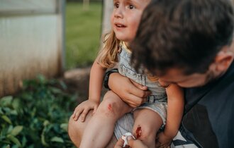 Kleines Mädchen mit einer blutenden Knieverletzug wird vom Vater versorgt.