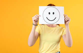 Woman,Hiding,Behind,Sheet,Of,Paper,With,Happy,Face,On