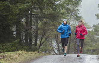 Ein Paar joggt bei schlechtem Wetter einen Waldweg entlang.
